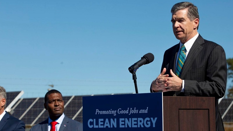 Governor Cooper stands at a rostrum next to a solar panel field to announce his Executive Order 80