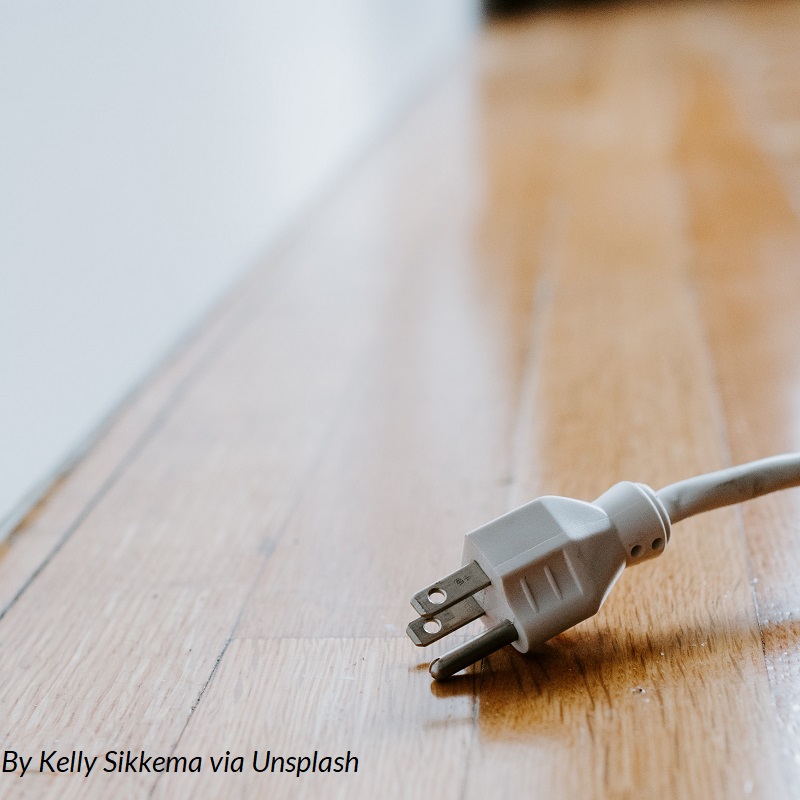 An electric plug lies on the floor near an outlet