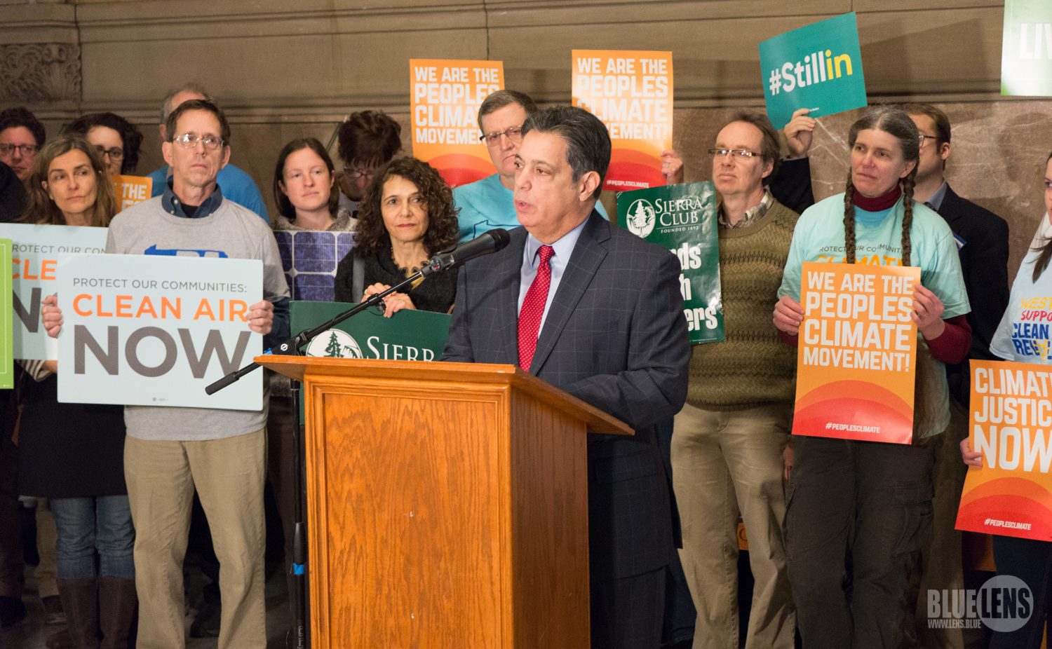 Senator Jay Costa speaks to a crowd and the media about the important of building a clean energy economy with a crowd holding signs behind him