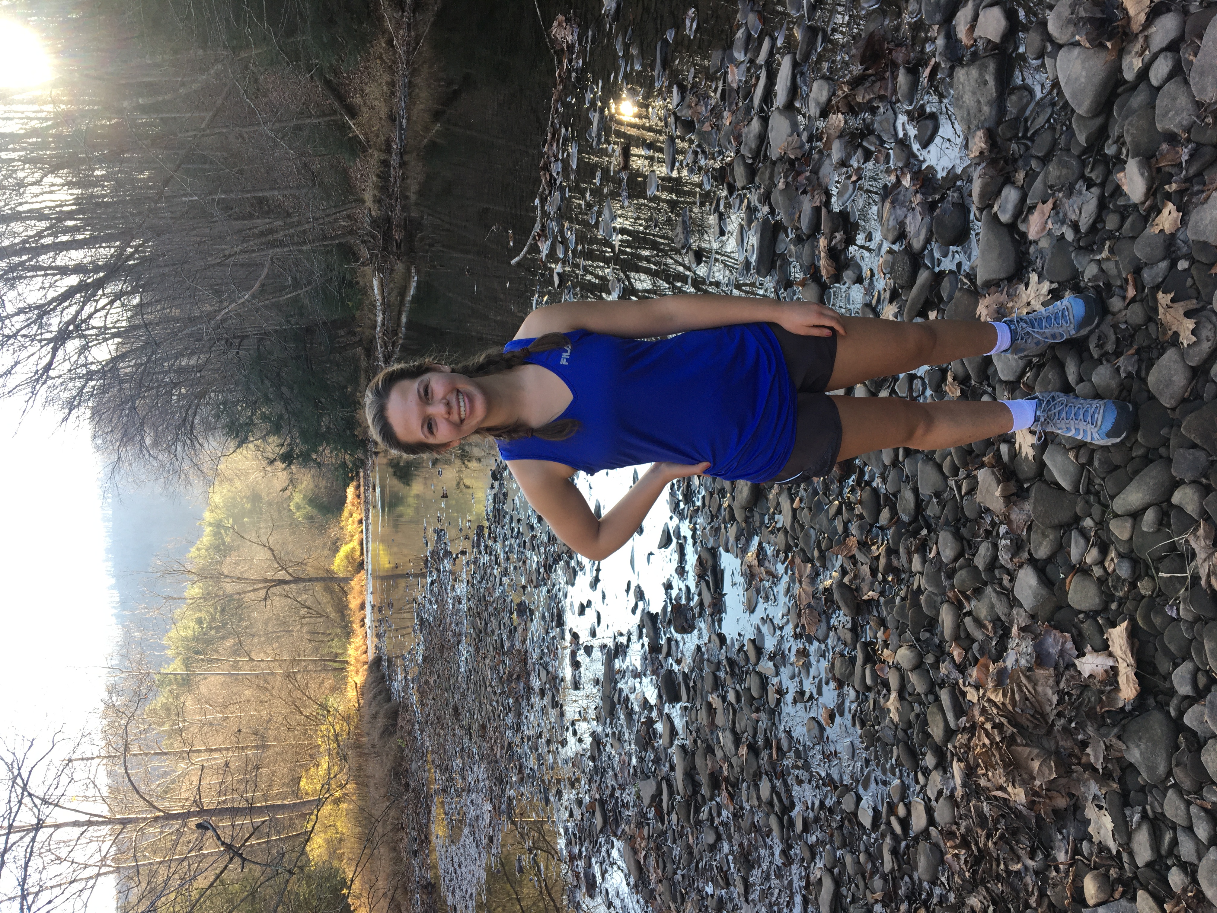 Caroline Weiss in a blue t-shirt and grey shorts standing on rocks next to a stream