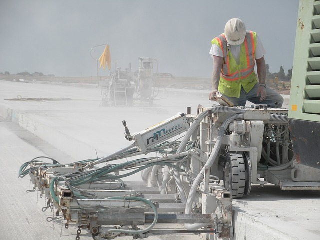 Construction worker focuses on concrete roadbed being constructed in heat and dust