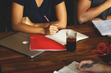 Torsos of three people meeting at a table with paper, pens, laptops, and beverages