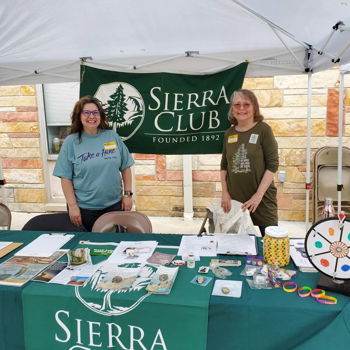Two women are standing by a table outdoors with a banner reading Sierra Club Hoosier Chapter