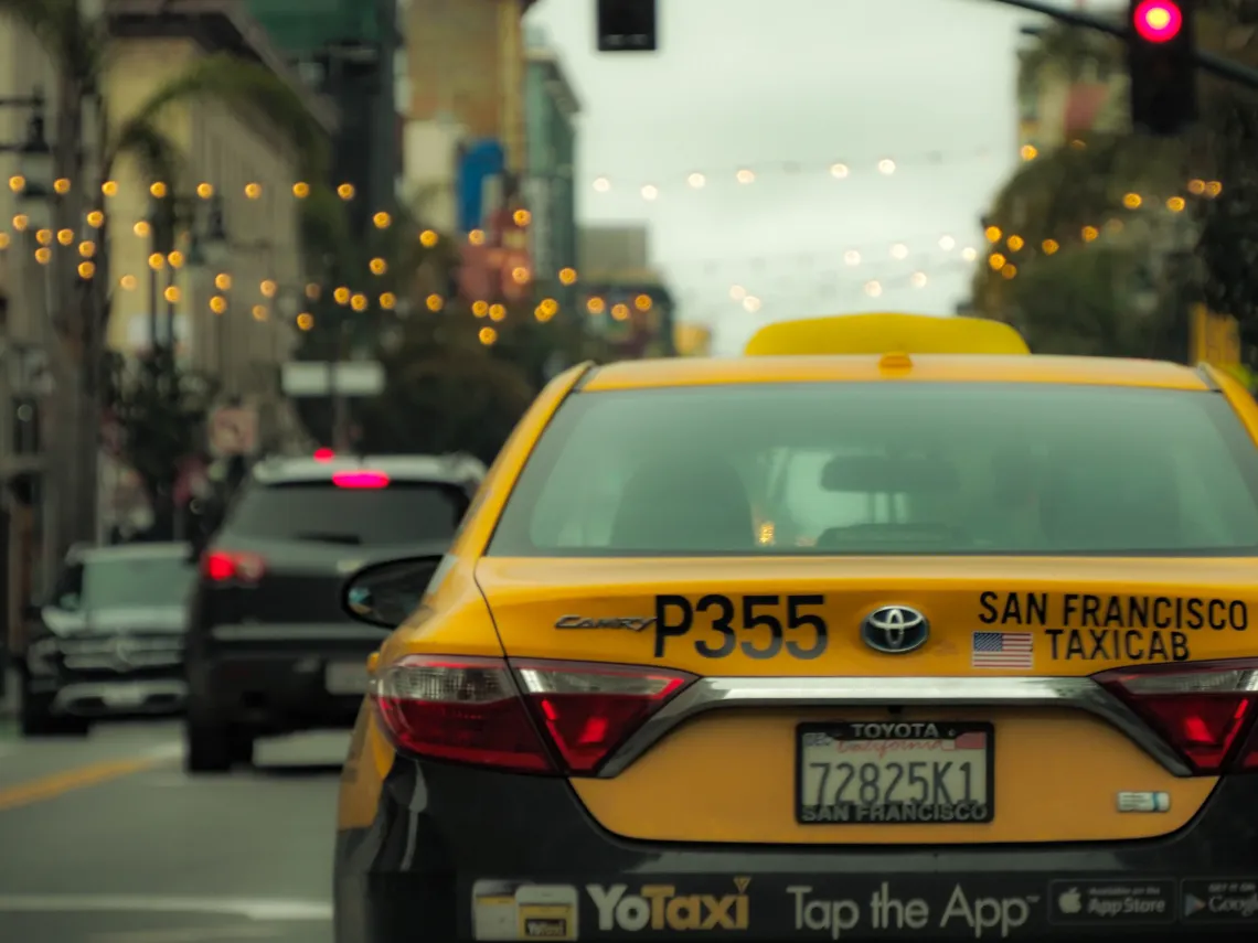 The back of a yellow San Francisco taxi cab against a blurred city background
