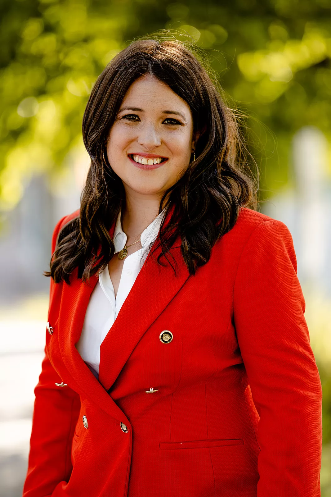Rebecca Barrett smiles on green natural background wearing red blazer