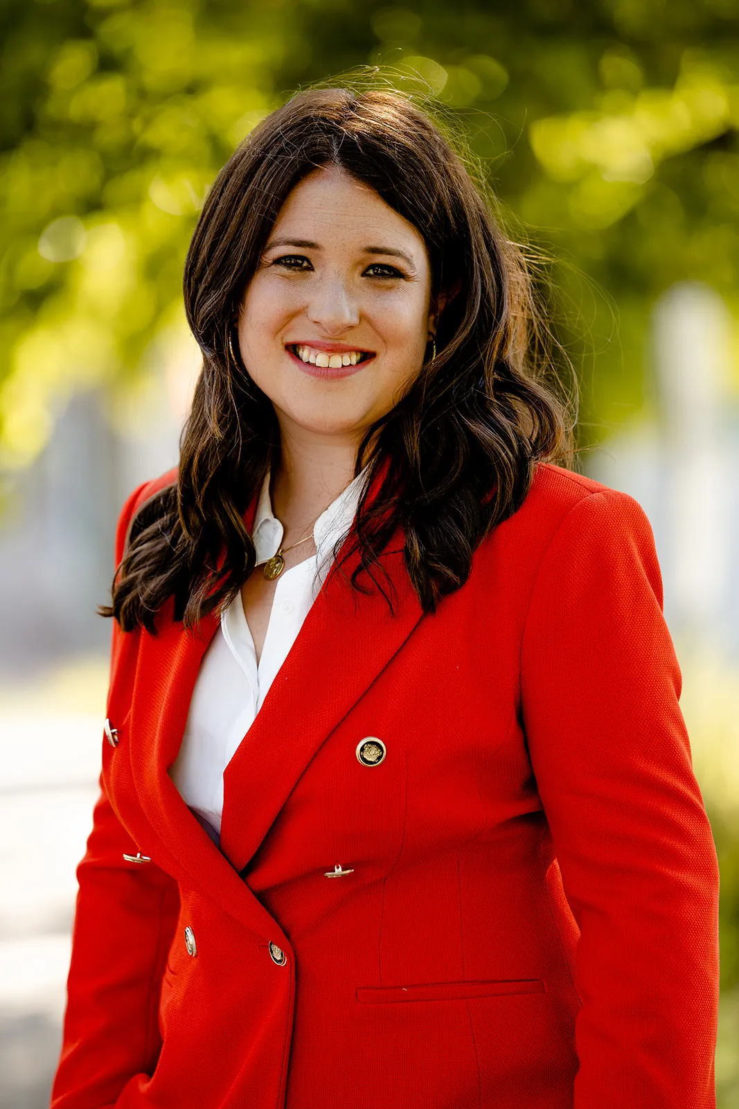 Rebecca Barrett smiles on green natural background wearing red blazer