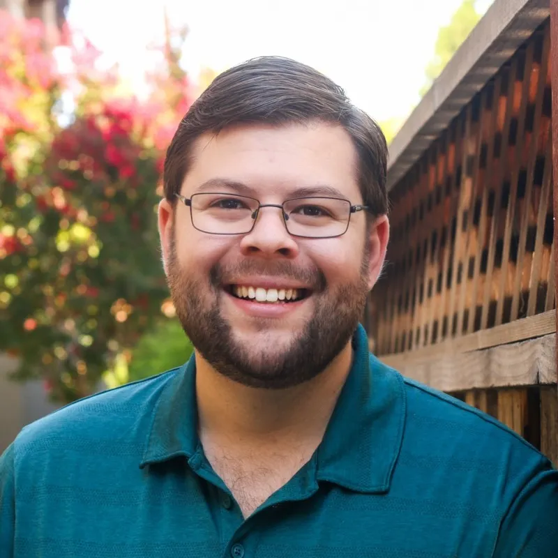 Jonathan T. Bash smiles in front of a fence ad garden background