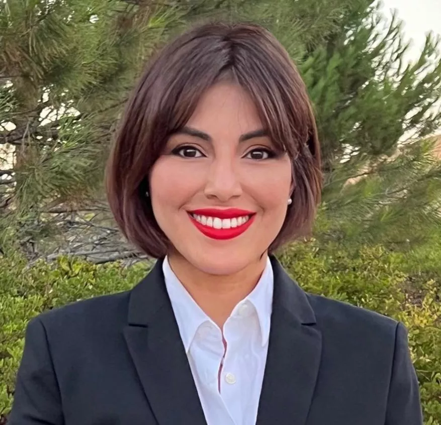 Marisol Rubio smiles wearing a black blazer on a green tree background