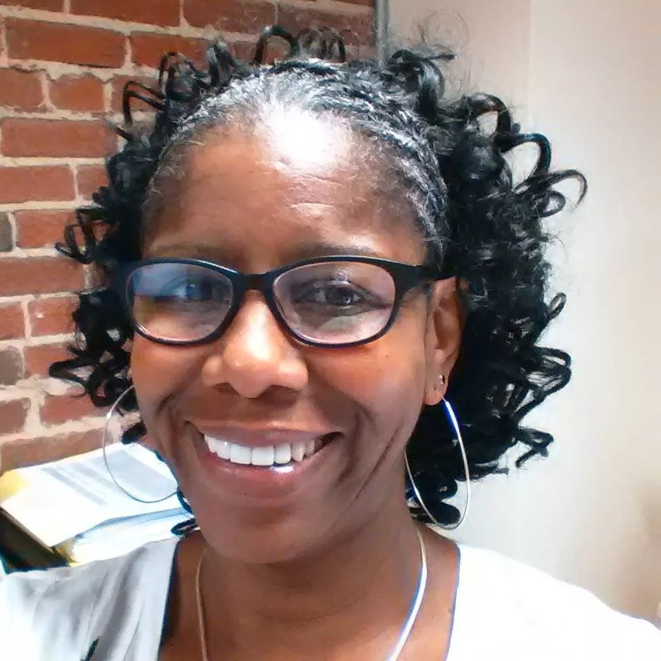 Kim-Shree Maufas smiles next to a brick wall