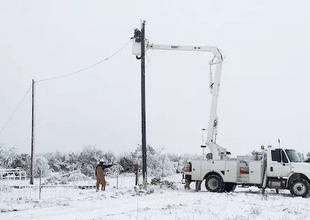 Linemen repair a utility line in a field covered with snow.