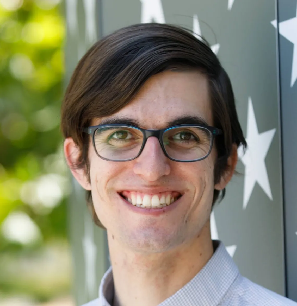 Steven Dunbar smiles against natural green and navy starred background