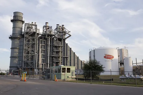 A fracked gas power plant and Austin Energy gas container surrounded by blue sky and clouds.