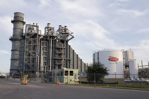 A fracked gas power plant and Austin Energy gas container surrounded by blue sky and clouds.