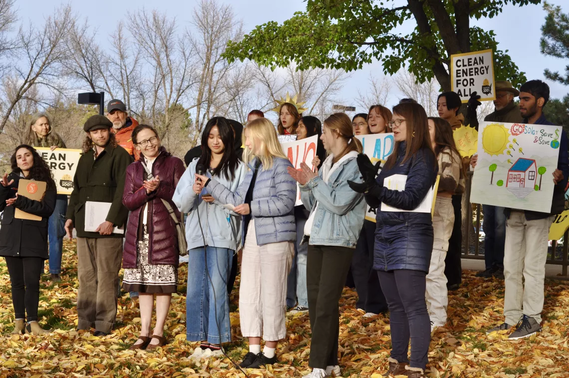 Picture of people standing outside at press conference, people with "Clean Energy for All" signs