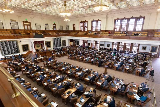 A view of policymakers sitting at desks on the floor of the Texas House of Representatives as seen from the balcony.