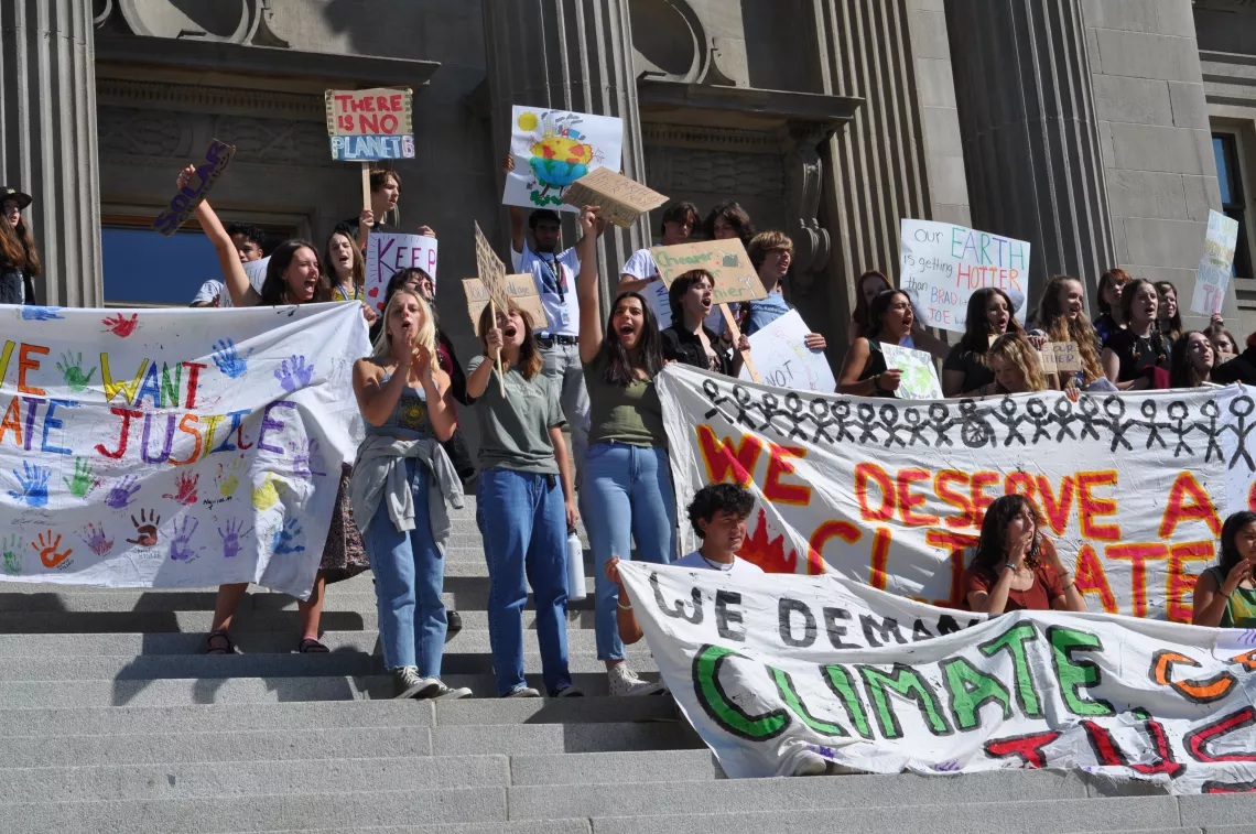 group of youth activists cheering and holding banners and signs at a rally for climate justice on the steps of the Idaho Capitol Building
