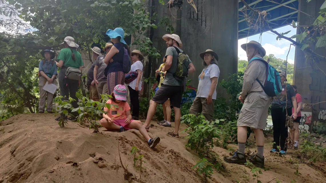 Group of people gather under a bridge on a sandy hill 