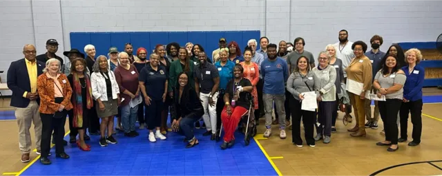 A few dozen people gather in a gym 