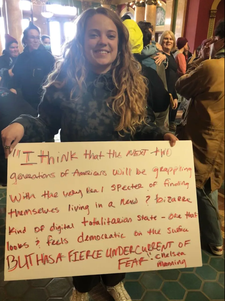 A person with long hair holds a sign