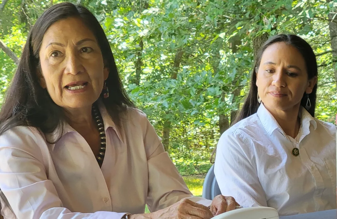 Two women side by side with green trees in background