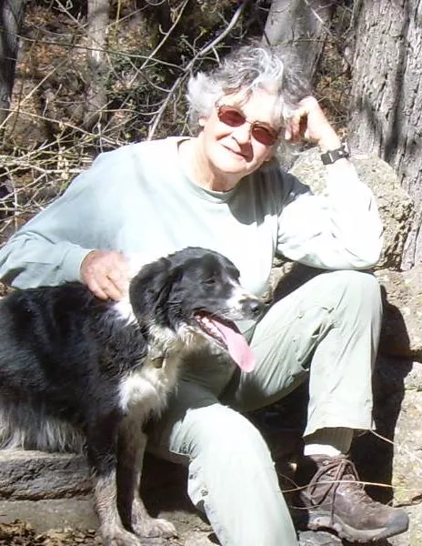 woman in jeans and hiking boots sitting in woods with black and white dog