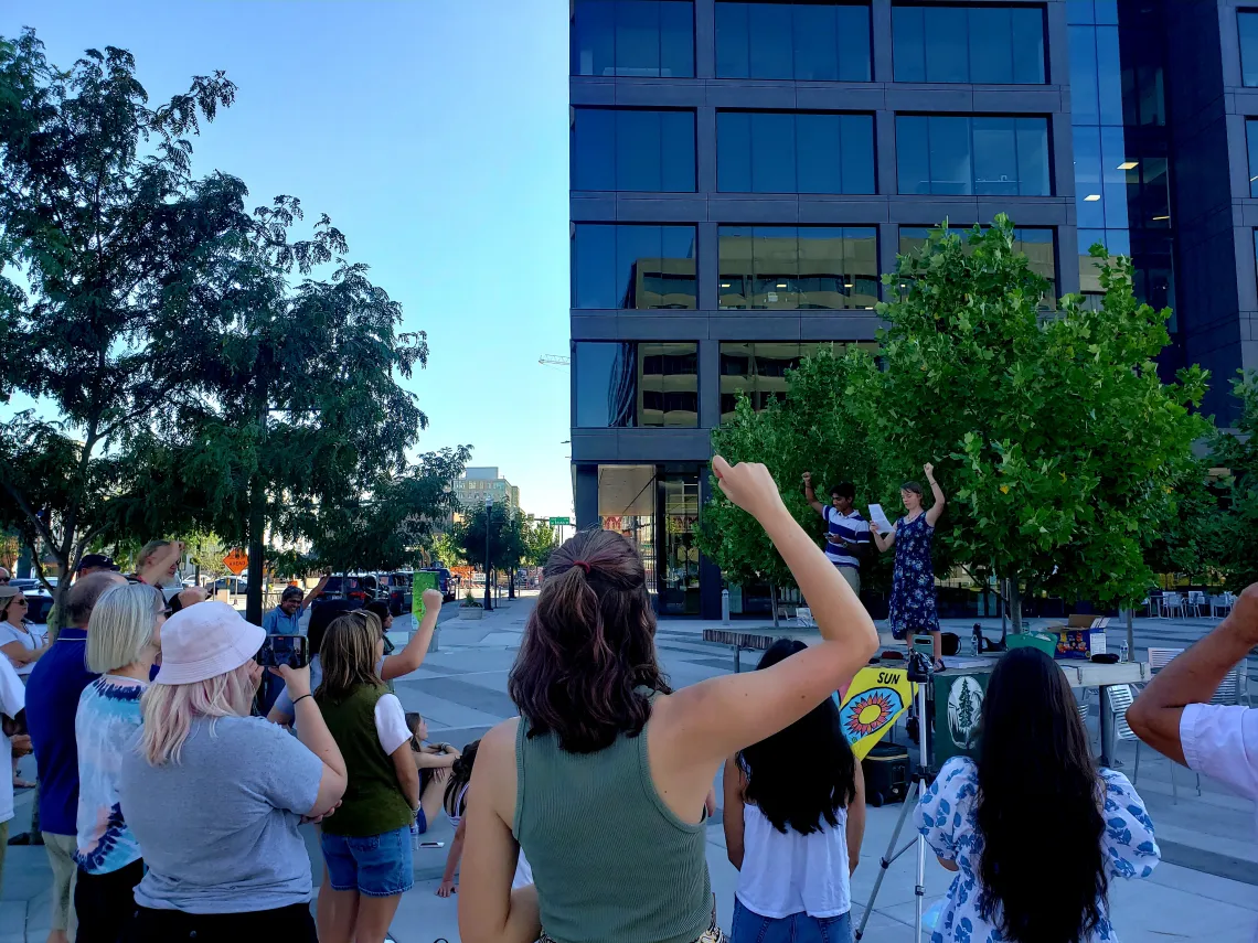 People raising their fists in the air at an outdoor community event, high school students speaking on top of an outdoor table