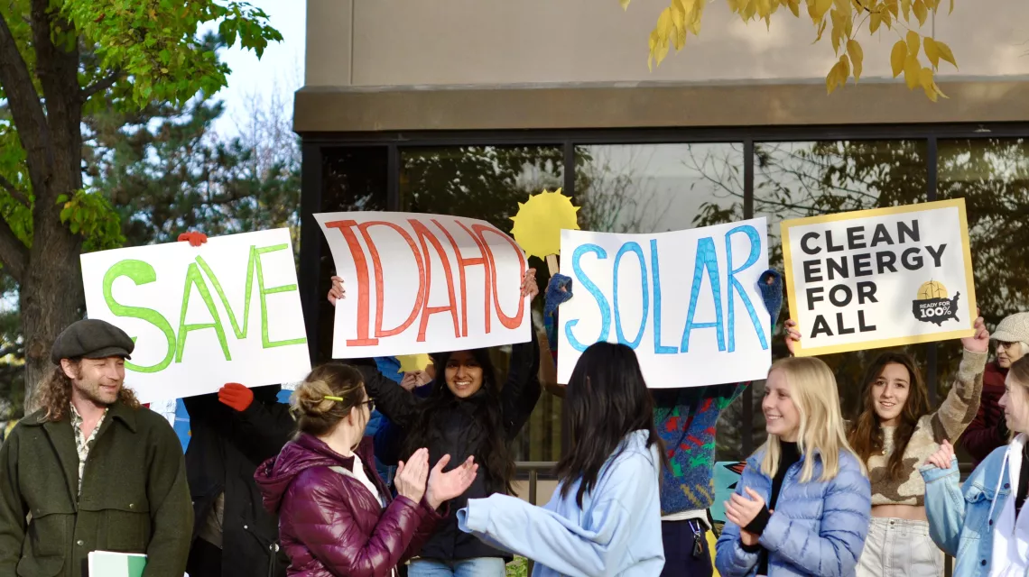 PIcture of young people holding up signs that say "Save Idaho Solar" and "Clean Energy for All" at a rally