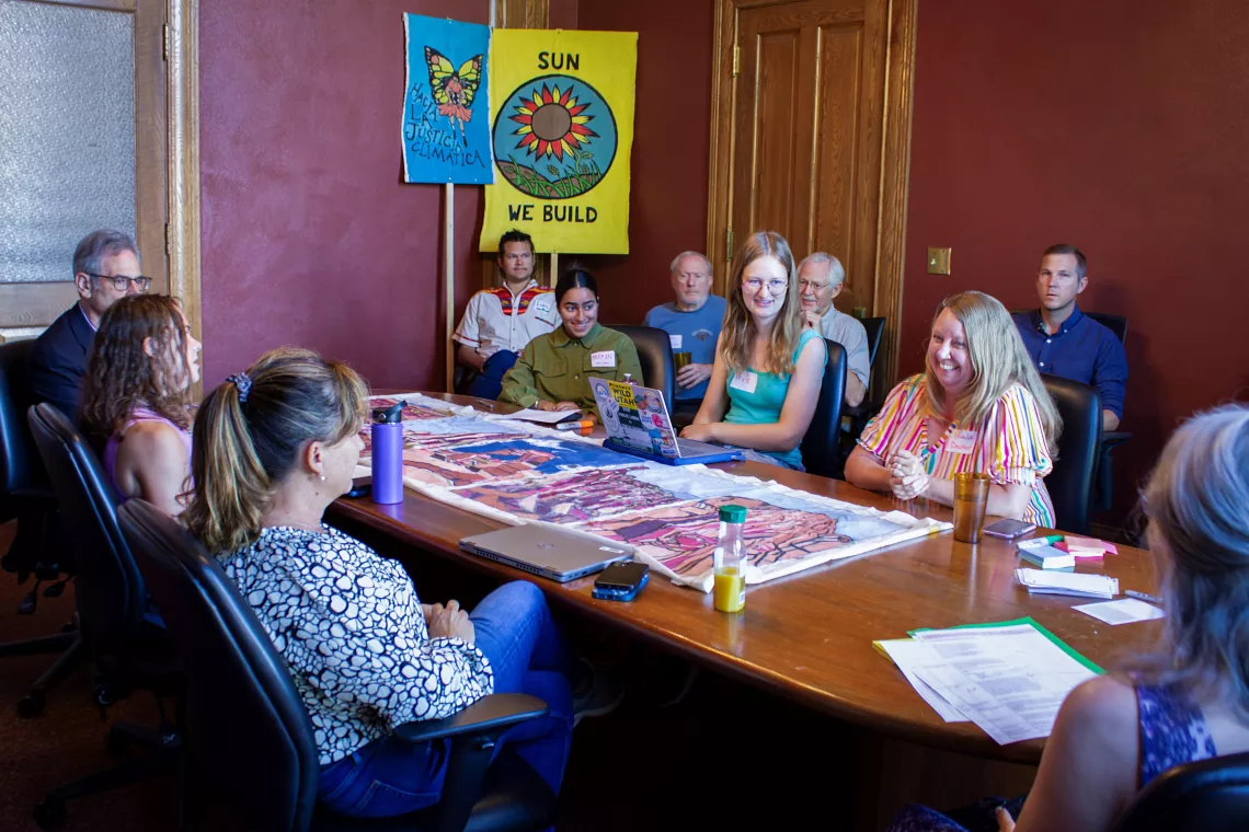 Clean Air Activists gather around a long table facing EPA Region 8 Administrator, KC Becker and her team with signage supporting a healthy planet behind them
