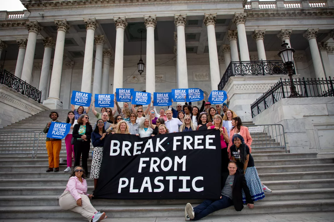 A group of people stand in front of a government building holding a large sign that reads "Break Free From Plastic"