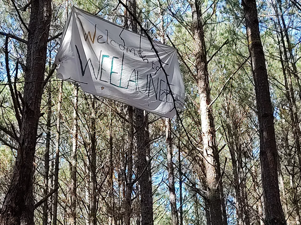 A banner proclaiming "Welcome to Weelaunee" hangs from some trees in Weelaunee Forest in Atlanta.
