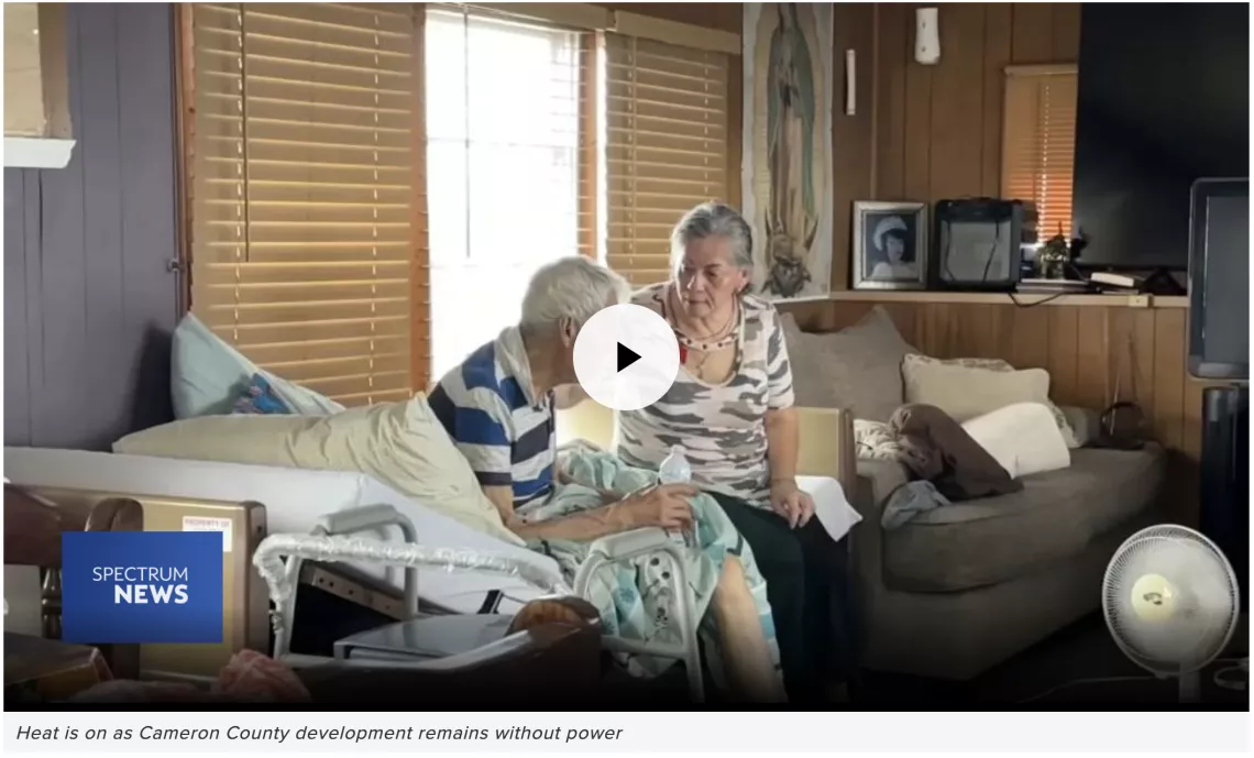 An older couple sits on a couch in a dark home.