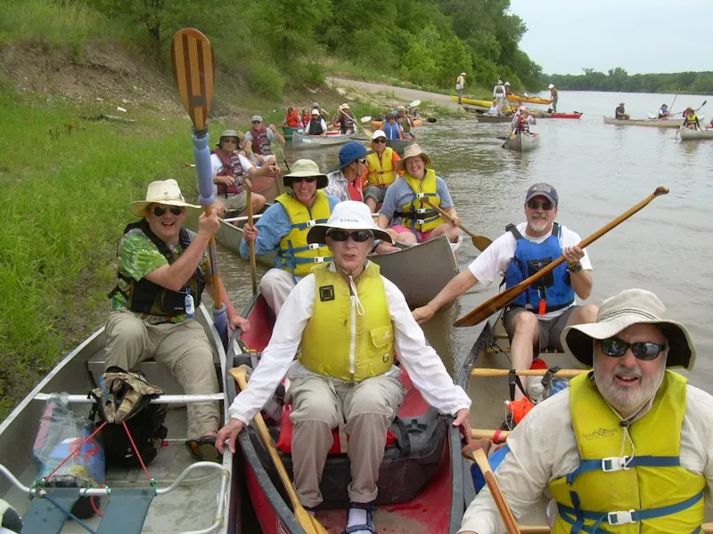 men and women wearing life jackets in canoes at river bank