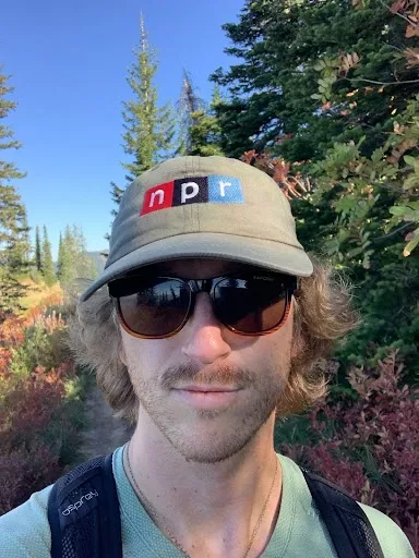 Tyler wearing sunglasses and a hat on a trail in the forest.
