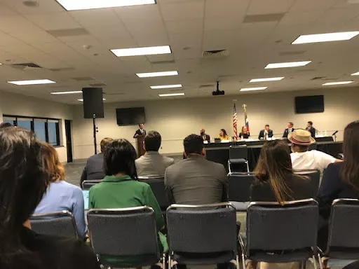 A panel of officials sit at the front of a hearing room