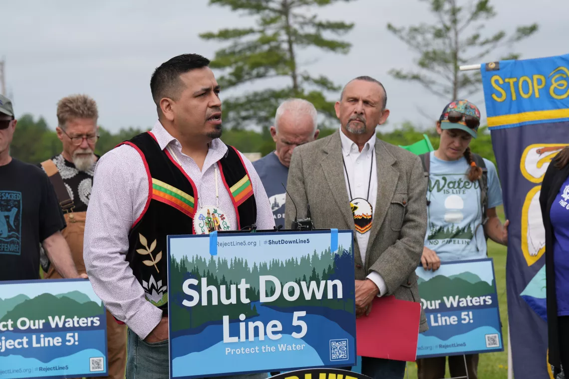 Dan Wiggins Jr. of the Bad River Band speaking at a press conference behind a sign that says "Shut Down Line 5". Photo credit: Devon Cupery