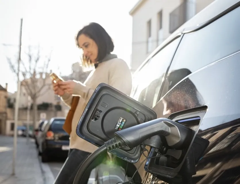 Woman charging electric vehicle and browsing her phone