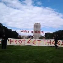 Protest signs reading "Water is Sacred. Protect the..."