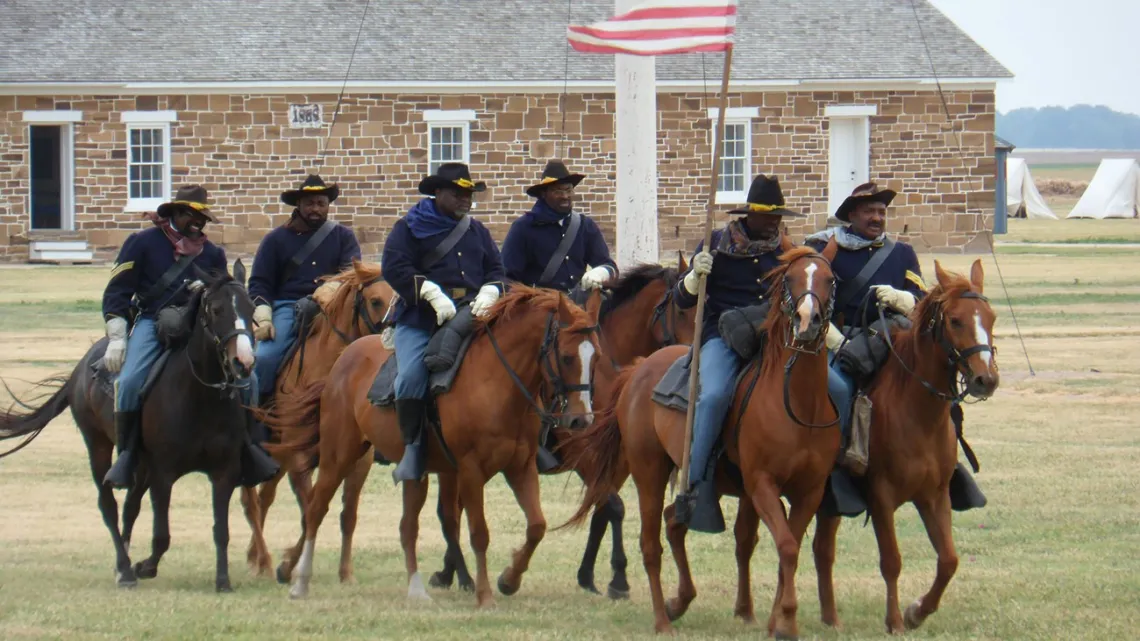 Black men dressed as soldiers on horses in front of stone building
