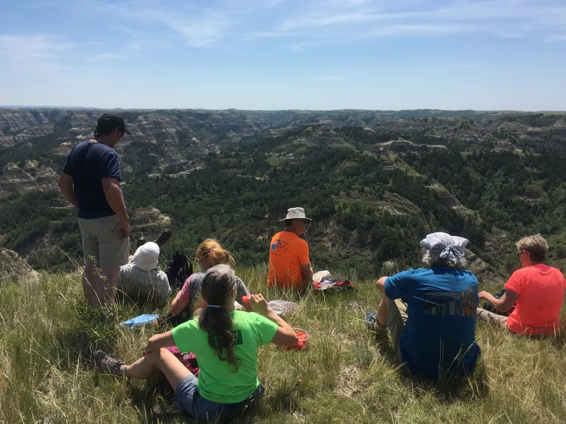 People resting on a grassy hillside with rolling hills and the horizon in the background