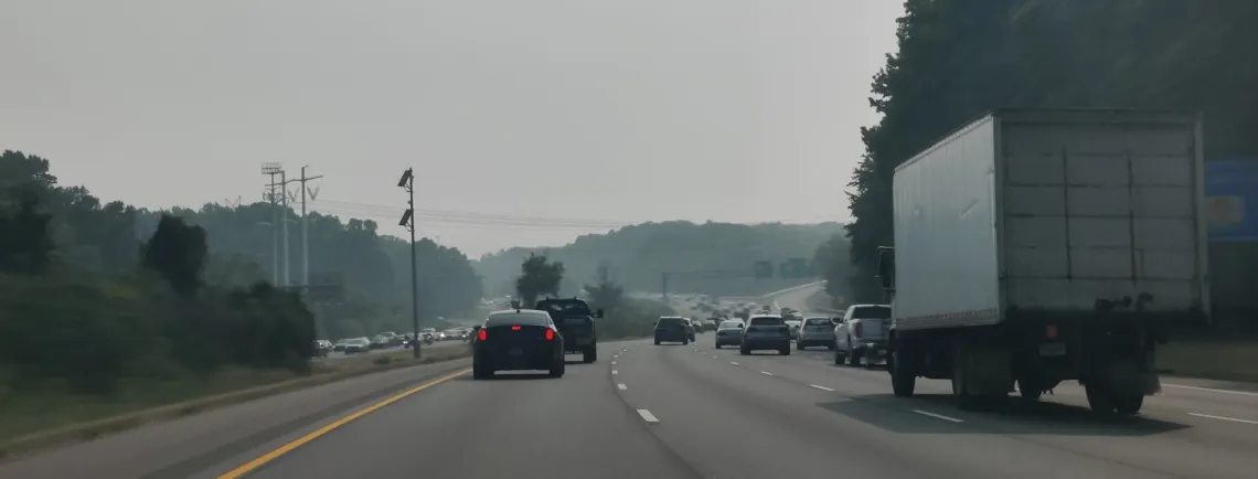 Cars and trucks move down a 3 lane highway in both directions on a smog filled day