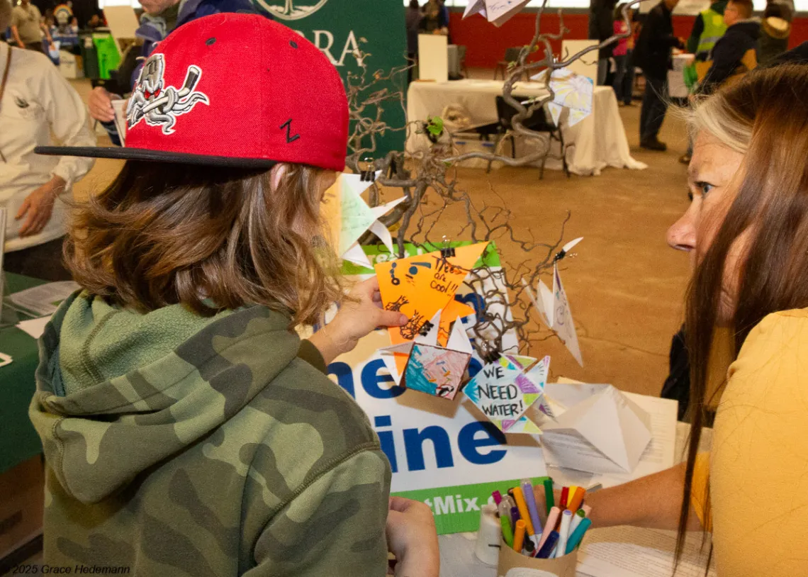 A child and a volunteer work together on an origami fish for Fish for the Future