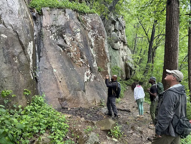 a group of three men and one teenage girl look up at the mountain they are hiking