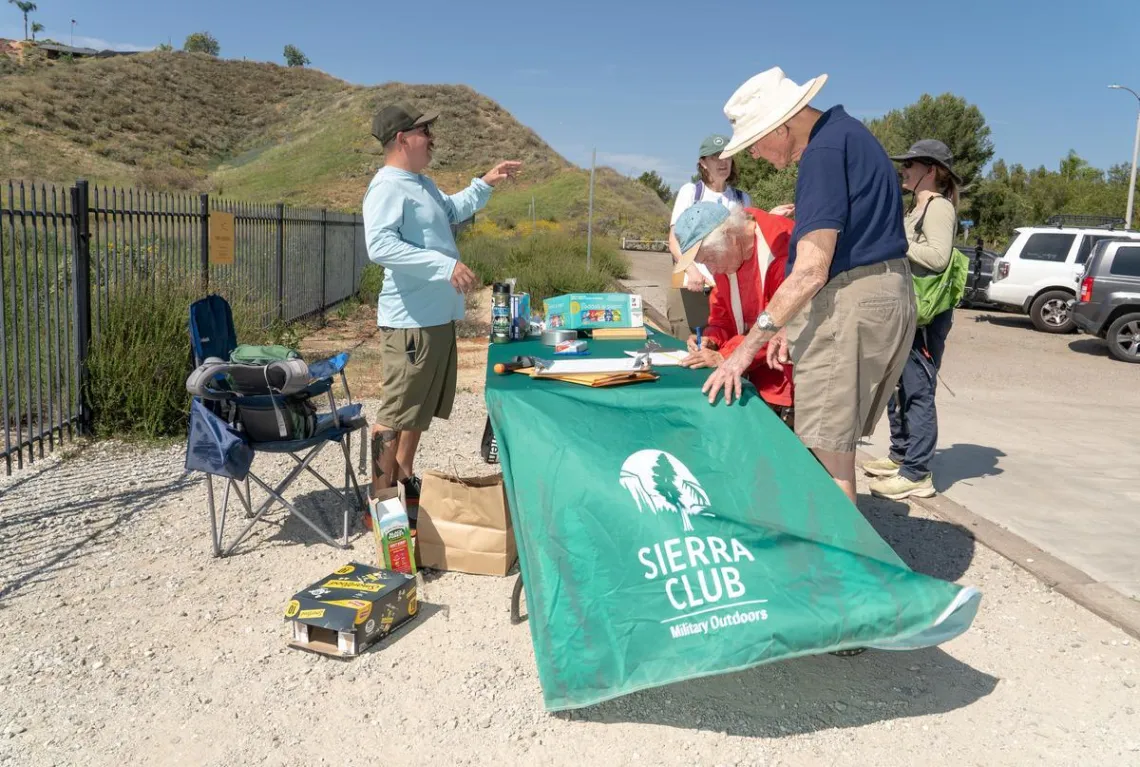 people check in at a table with a banner that says Sierra Club Military Outdoors