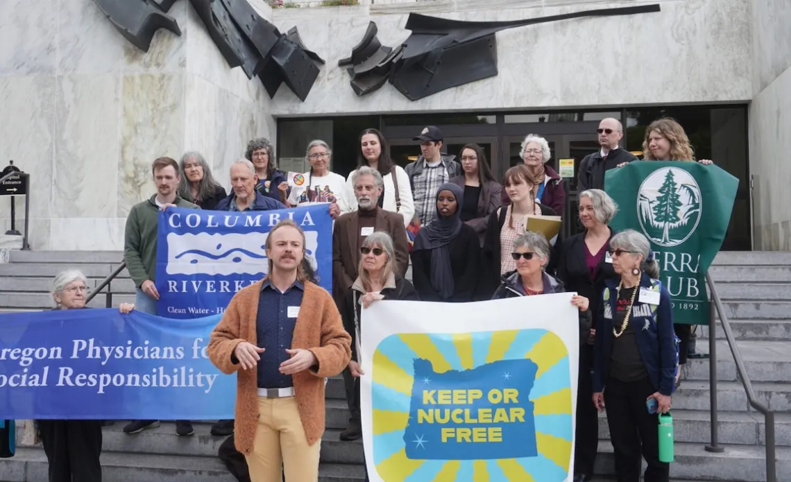 A group of people holding various signs stands on a large stone staircase in front of the Oregon capitol building.