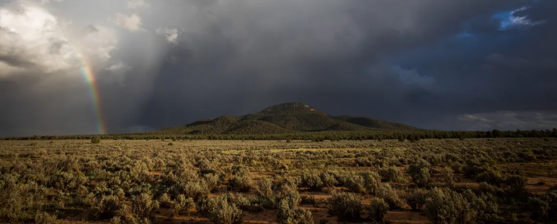 A rainbow next to a mountain on a stormy day. 