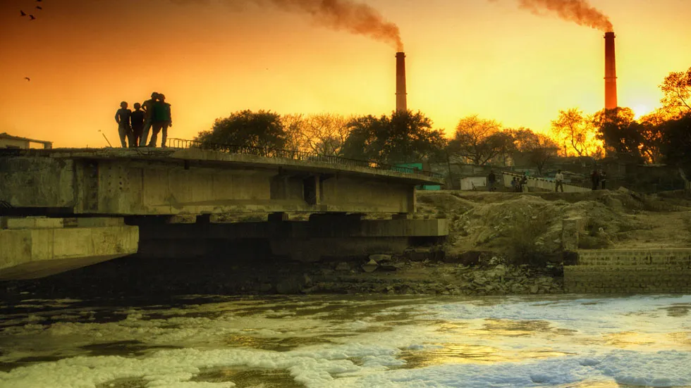 Smokestack against evening sky, river with foamy water in front
