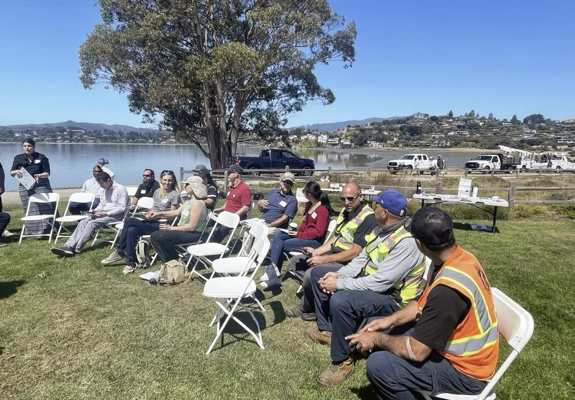 People sit on chairs on grassy field next to water