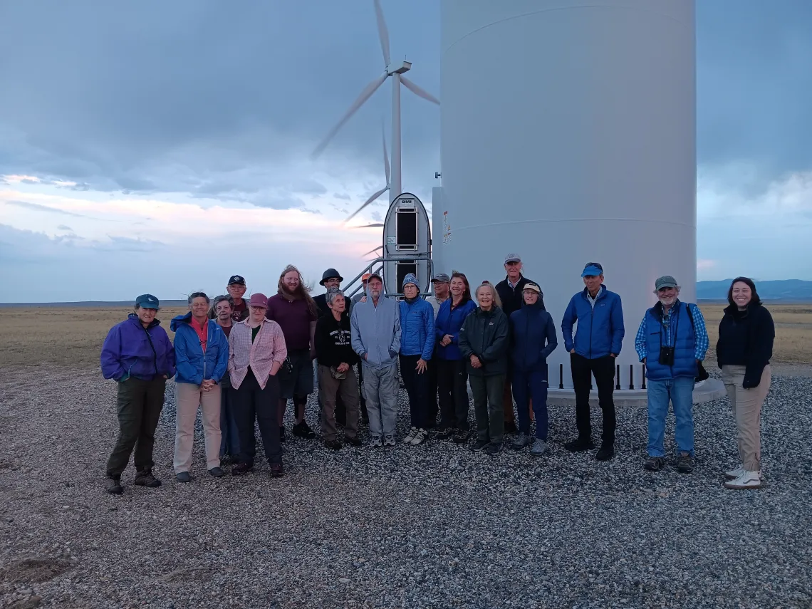 A group of people pose in front of a wind turbine.