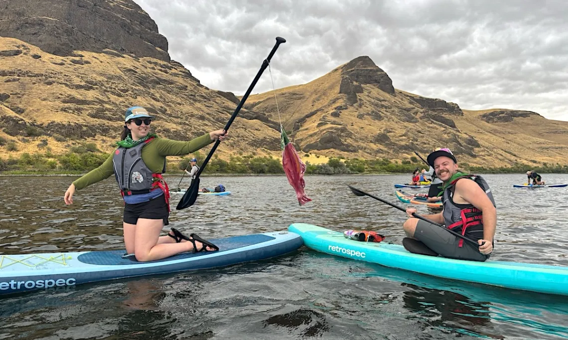 Two people sit on paddle boards on a river