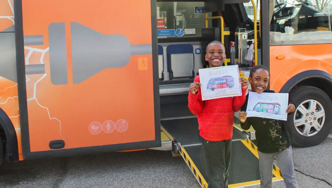 Two kids pose with drawings in front of MVTA's electric mini-bus